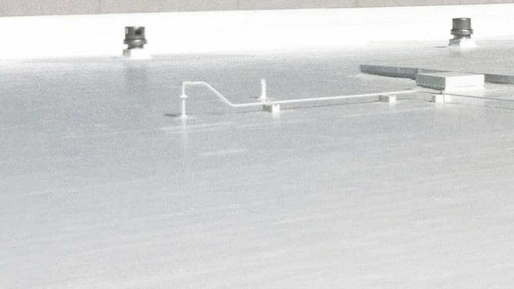 Spacious flat roof with a reflective white coating, featuring several protruding ventilation ducts and pipes.