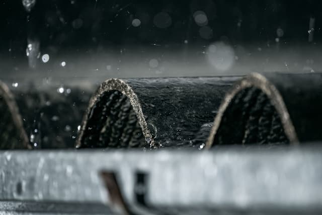 Rain falling on dark roof tiles above a metal gutter