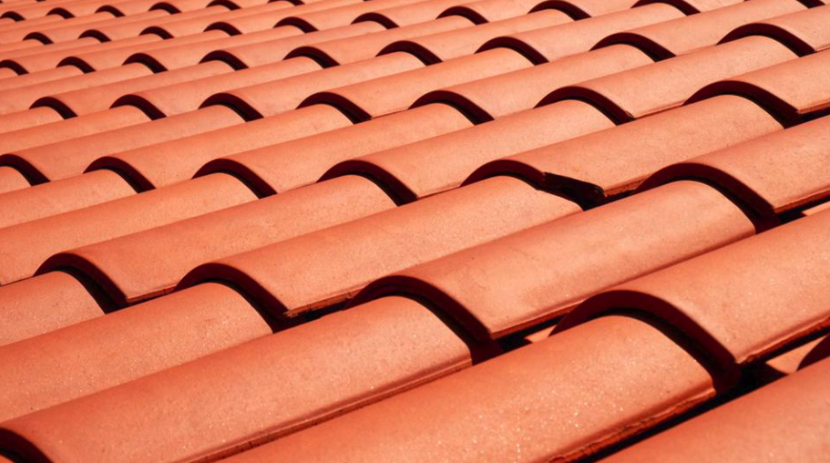 Pattern of vibrant terracotta clay curved roof tiles in a repeating pattern, highlighted by sunlight creating a play of light and shadow.