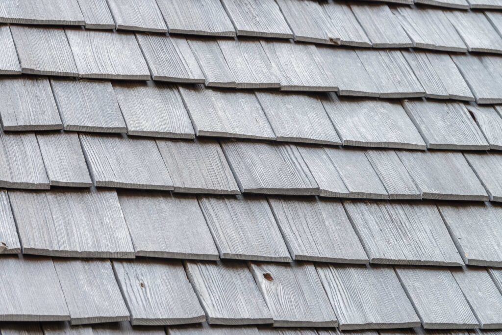 Detailed view of grey wooden roof shingles arranged in an overlapping pattern, providing a background and texture characteristic of residential roofing materials.