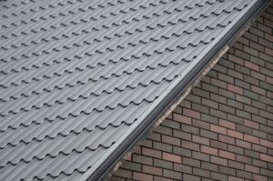 Diagonal composition of grey metal roof tiles meeting a wall with red and black brick pattern, showing the contrast between the two textures.