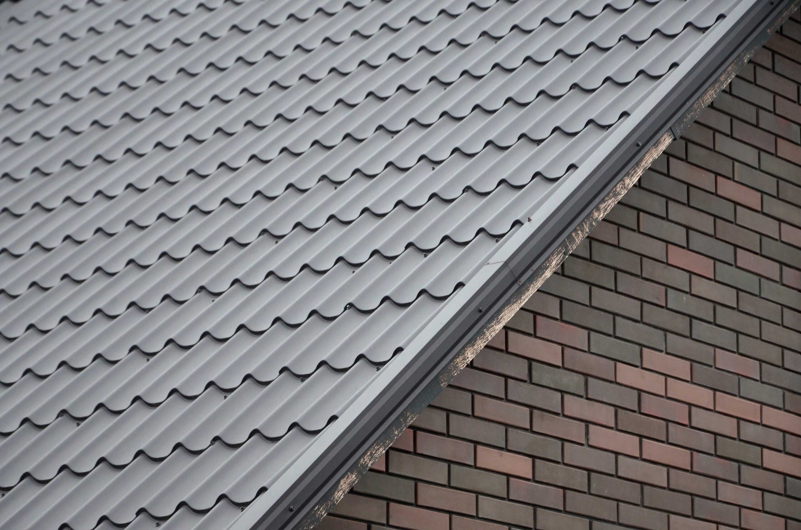 Diagonal composition of grey metal roof tiles meeting a wall with red and black brick pattern, showing the contrast between the two textures.