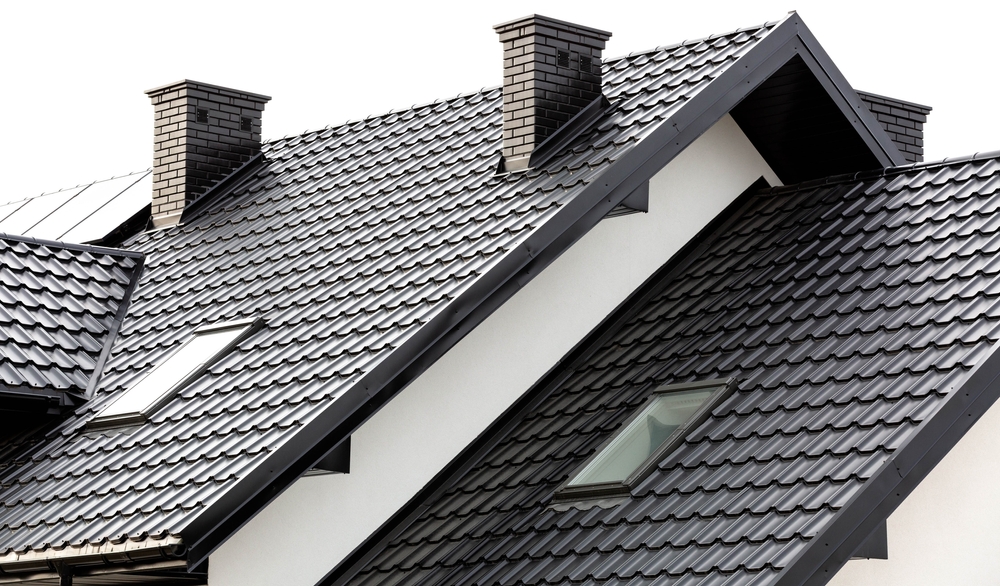 Architectural detail of a modern house with steep grey tiled roofs, featuring dormer windows, skylights, and brick chimneys.