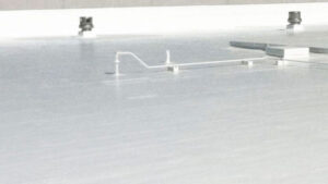 Spacious flat roof with a reflective white coating, featuring several protruding ventilation ducts and pipes.