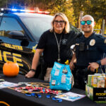 Helotes Police Department officers smiling at their booth during the Kinetic Kids Family Unite Night in Helotes, Texas. Title: Helotes Police supporting Kinetic Kids event
