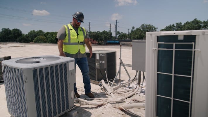 Anthony Beard inspecting conduit and line sets around rooftop HVAC units