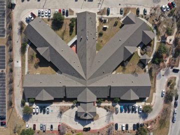 Overhead view of a large building with a distinctive star-shaped roof design, surrounded by parking lots with cars and landscaped areas.